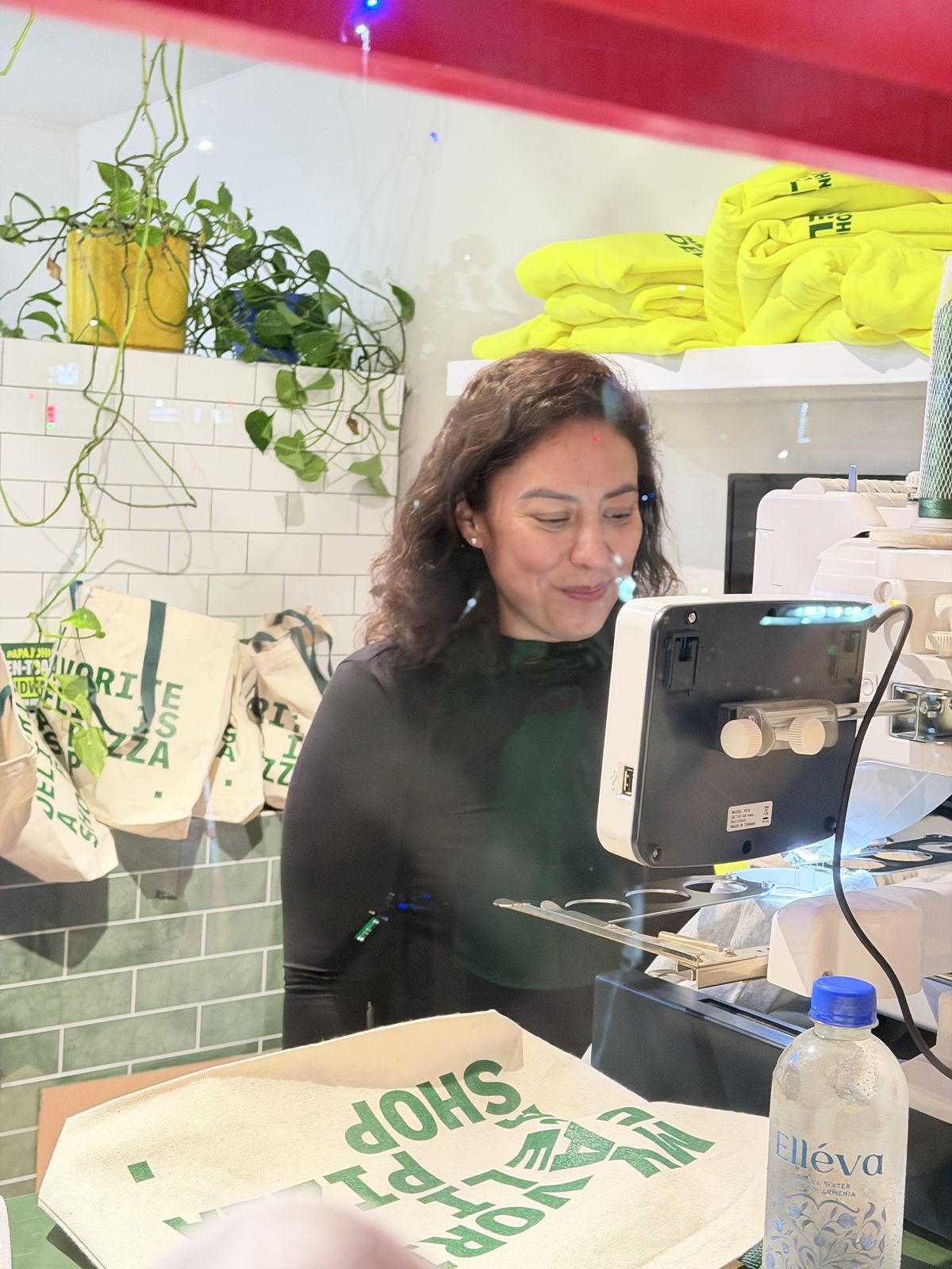 Crew member running an embroidery machine beside folded sweatshirts and tote gifts at a party