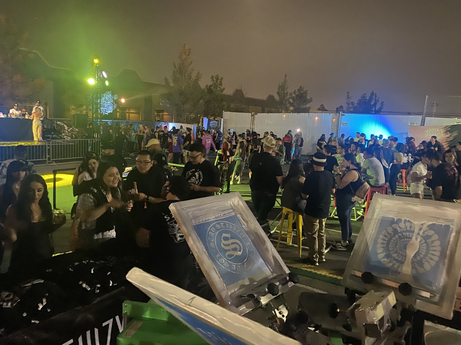 Evening party crowd mingling around a live customization station under string lights